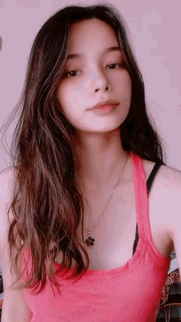 a woman with long hair is wearing a pink tank top