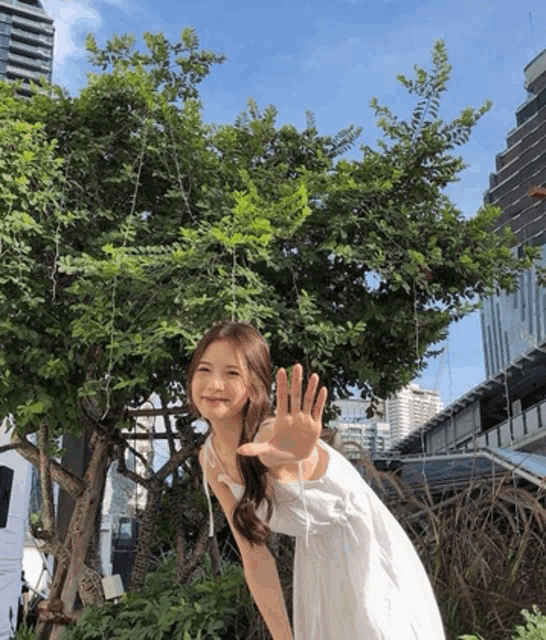 a woman in a white dress is waving her hand