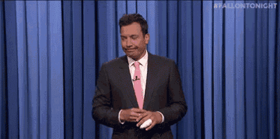 a man in a suit and tie is standing in front of a blue curtain and making a funny face .