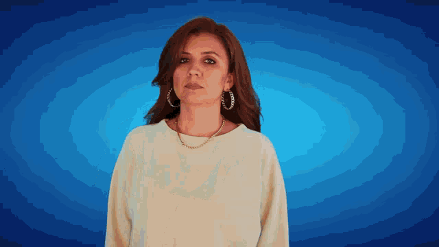 a woman wearing hoop earrings and a necklace looks at the camera