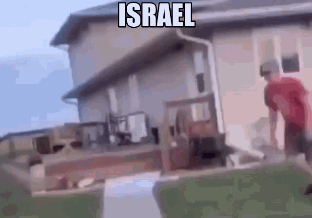 a man in a red shirt is standing in front of a house with the word israel on it .