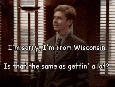a man in a suit and tie is standing in front of a window and says i 'm sorry