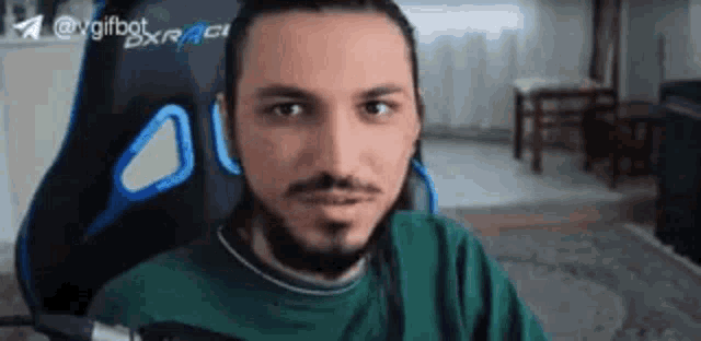a man with a beard is sitting in a gaming chair and making a funny face .