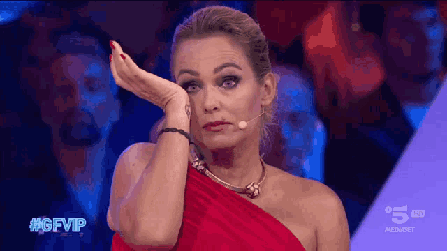 a woman in a red dress wipes her face with her hand in front of a microphone with the hashtag #gfvip