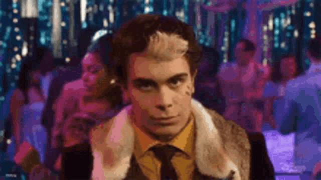 a man in a fur coat and tie is standing in front of a crowd of people .