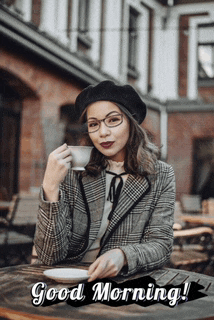 a woman is sitting at a table drinking a cup of coffee and says good morning !