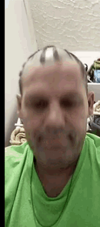 a man with a shaved head is wearing a green t-shirt and looking at the camera .