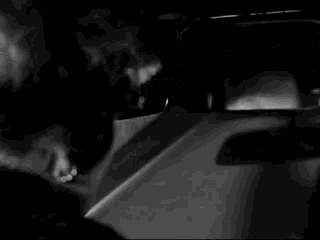 a black and white photo of a woman looking at her reflection in a rear view mirror
