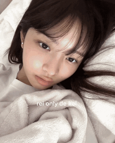 a woman laying on a bed with a white blanket that says rei only de kei on it