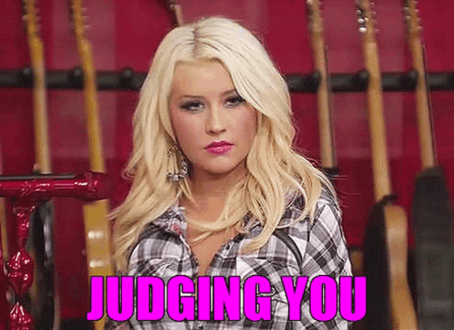 a woman in a plaid shirt is standing in front of a row of guitars and the words judging you are written in pink
