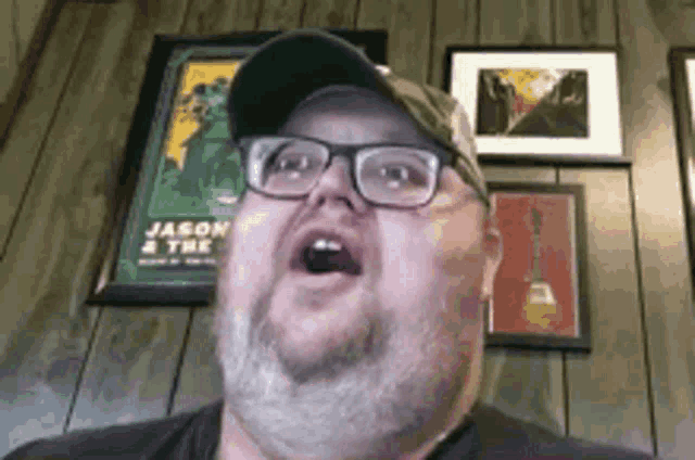 a man with glasses and a hat is making a funny face in front of a wooden wall .