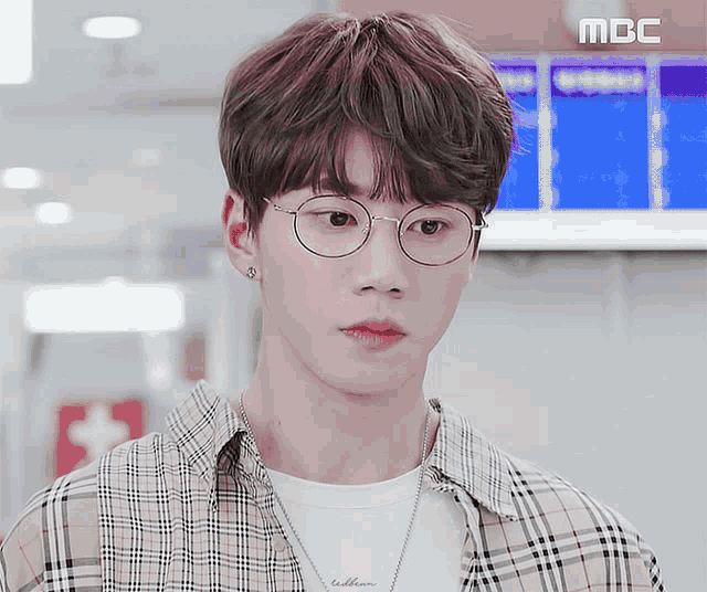 a young man wearing glasses and a plaid shirt is standing in front of a mbc advertisement