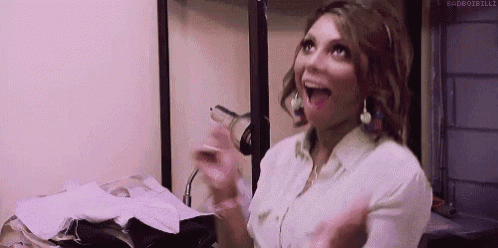a woman in a white shirt is standing in a room with a bunch of clothes and a hair dryer .