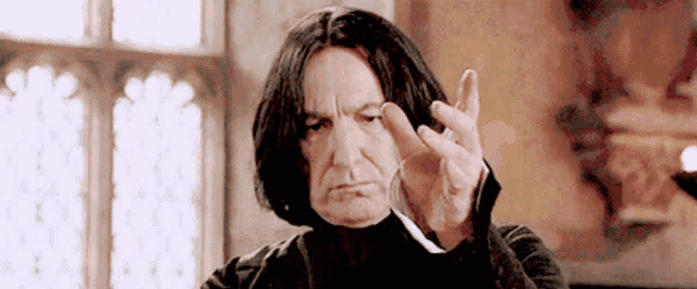 a man with long black hair is making a funny face while holding a wand in his hand .