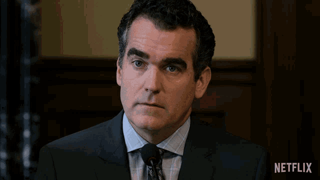 a man in a suit and tie stands in front of a microphone with a netflix logo in the corner