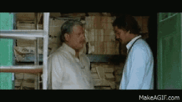 two men are standing next to each other and talking in a room filled with papers .