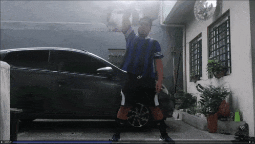 a man in a blue and black striped shirt is standing in front of a black car