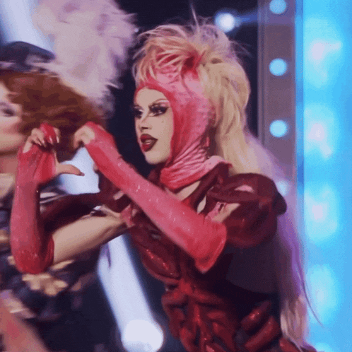 a woman in a red dress and pink gloves makes a heart with her hands
