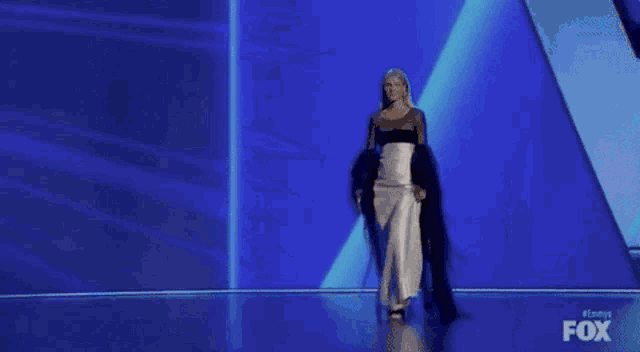 a woman in a white dress is walking on a stage with a blue background .