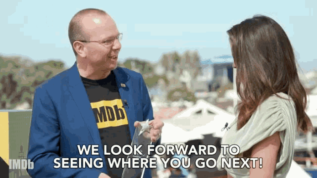 a man in a blue suit is talking to a woman who is wearing a t-shirt that says imdb