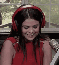 a woman wearing red headphones and a red dress is smiling in front of a microphone .