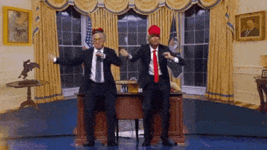 two men in suits and ties are dancing in front of a desk