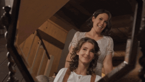 two women are standing next to each other and smiling in front of a mirror