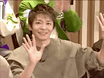 a man in a green jacket is waving at the camera while sitting in a chair .