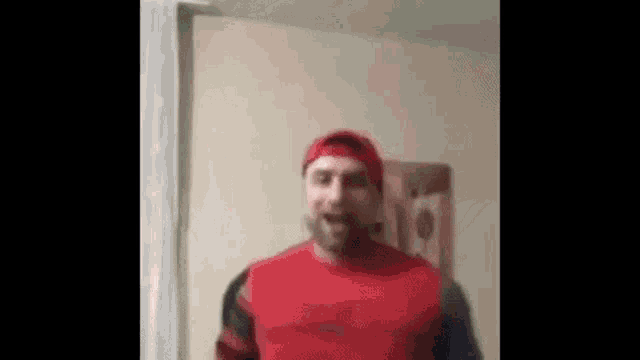 a man wearing a red shirt and a red hat is standing in a living room .