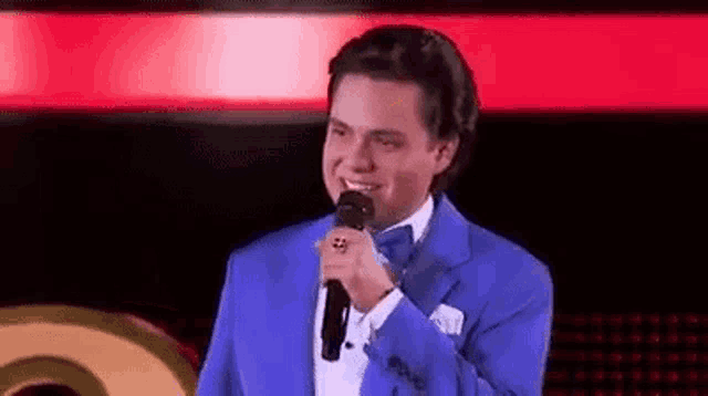 a man in a blue suit is singing into a microphone .
