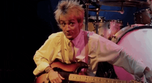 a man playing a guitar in front of a pink drum set