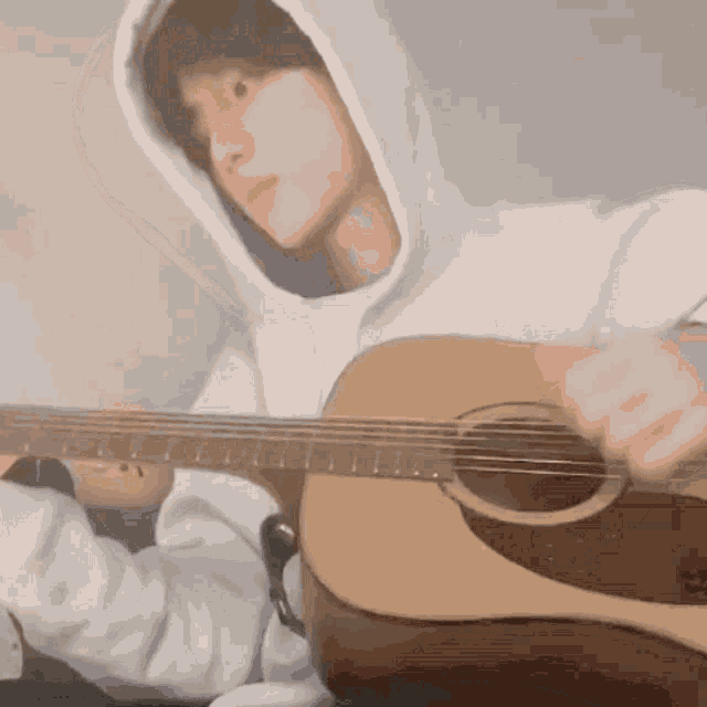 a man in a white hoodie playing an acoustic guitar