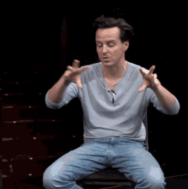 a man in a blue shirt and jeans is sitting in a chair with his hands outstretched