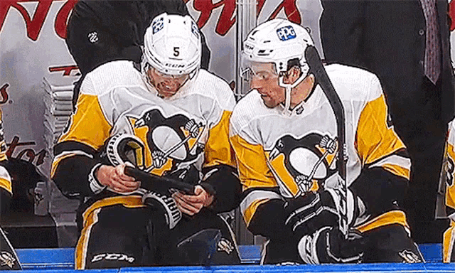 two hockey players are sitting on the bench and one has the number 5 on his helmet .