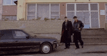 two men are walking in front of a car with a bmw logo on the wheel