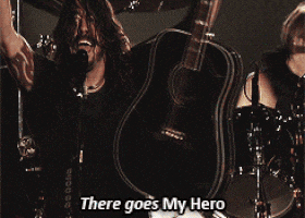 a man singing into a microphone while holding a guitar with the words " there goes my hero " above him