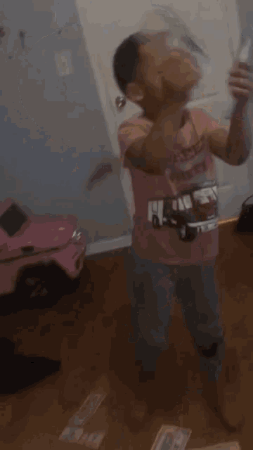 a young boy wearing a pink shirt with a car on it is holding a bottle