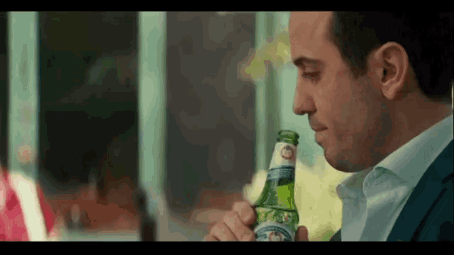 a man in a suit is drinking from a bottle with a label that says ' s.pellegrino ' on it