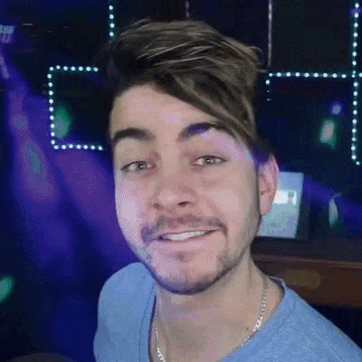 a man with a beard wearing a blue shirt and a chain around his neck is smiling .