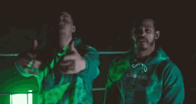two men in green hoodies are pointing at something