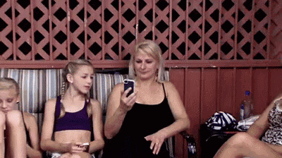 a woman is looking at her cell phone while sitting next to a group of girls .