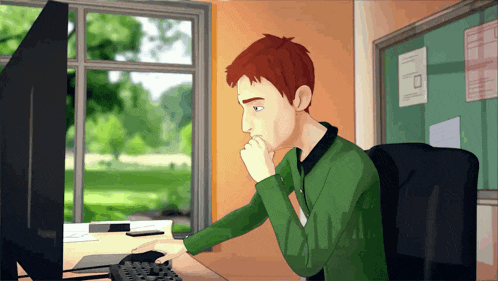 a man in a green sweater sits in front of a computer monitor