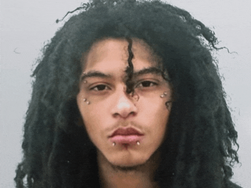 a young man with dreadlocks and piercings on his face looks at the camera