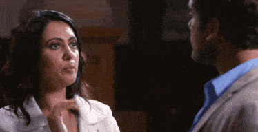 a woman in a white coat looks at a man in a blue shirt in a dark room