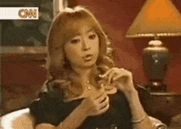 a woman is sitting on a couch with her hands on her chest and a lamp in the background .