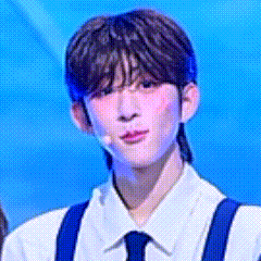 a young man wearing a white shirt and blue suspenders is standing in front of a microphone on a stage .