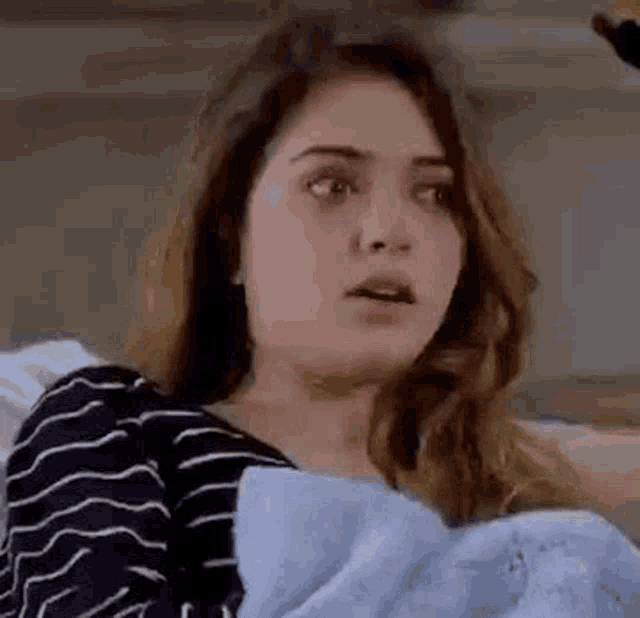 a woman is sitting on a couch with a blue blanket and making a funny face .