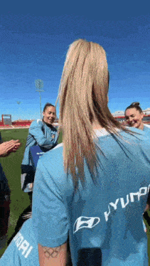 a woman wearing a blue hyundai shirt is standing on a field
