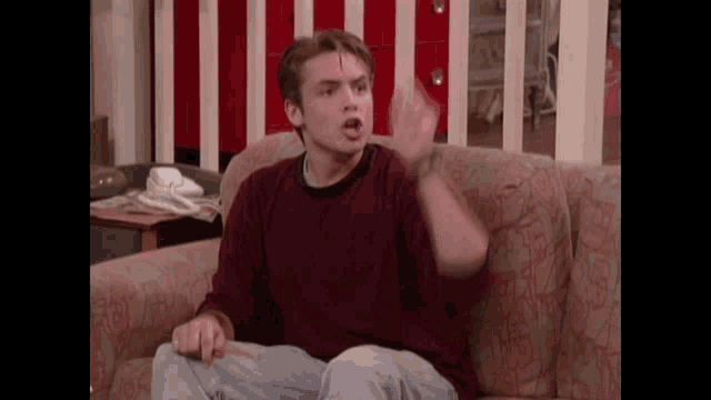 a young man is sitting on a couch making a funny face while holding a cigarette .