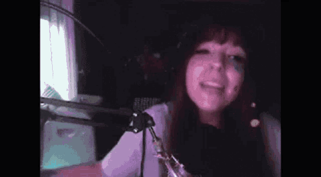 a woman is standing in front of a microphone in a dark room and smiling .